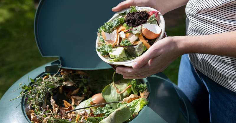 Close Up Of Woman Emptying Food Waste Into Garden Composter At Home