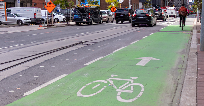 Green bike lane on a busy street in downtown Toronto as a cyclist is seen in the distance.