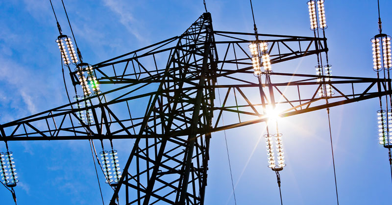 high voltage power pylons against blue sky and sun rays