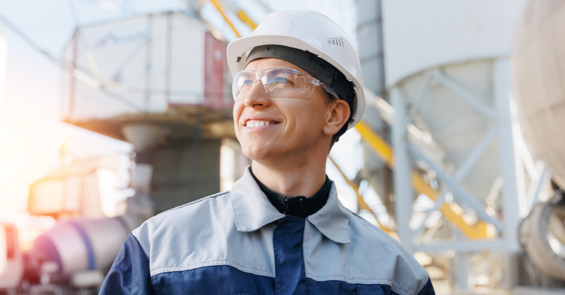Portrait happy male engineer of concrete factory, young man in uniform with hard hat on background cement mixer truck.