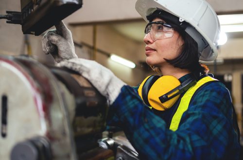 A-woman-engineer-in-a-blue-plaid-shirt-and-yellow-safety-gear-is-working-on-a-machine
