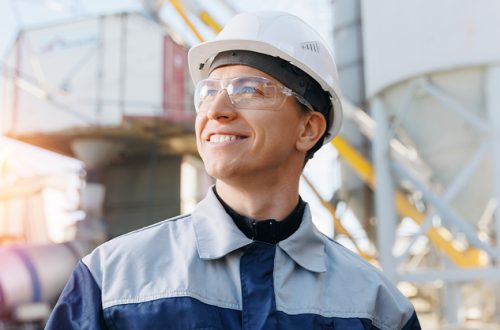 Portrait happy male engineer of concrete factory, young man in uniform with hard hat on background cement mixer truck.