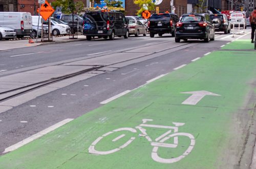 Green bike lane on a busy street in downtown Toronto as a cyclist is seen in the distance.