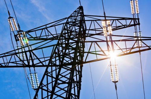 high voltage power pylons against blue sky and sun rays